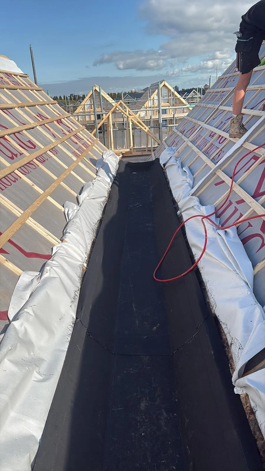 Kilgoot met zwarte dakbedekking tussen twee nieuwe hellende daken in aanbouw